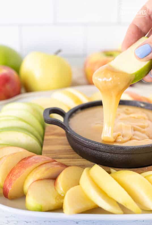 Hand holding a slice of apple with caramel dip drizzling off the end.