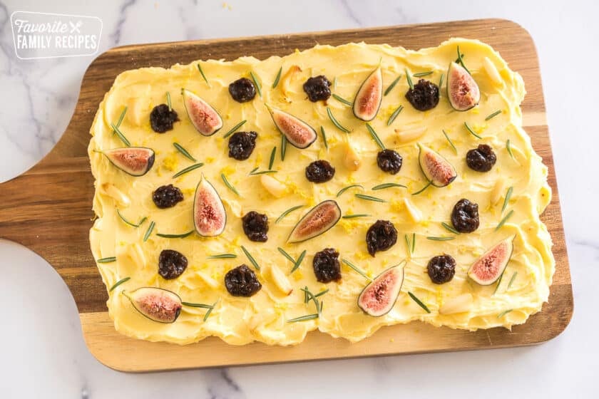 butter smeared on a wooden slab topped with lemon zest, salt, figs, fig butter, rosemary and roasted garlic