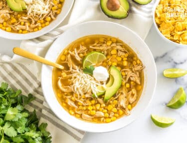 a bowl of chicken tortilla soup topped with lime, sour cream, cheese, and avocado