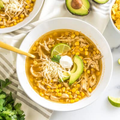 a bowl of chicken tortilla soup topped with lime, sour cream, cheese, and avocado