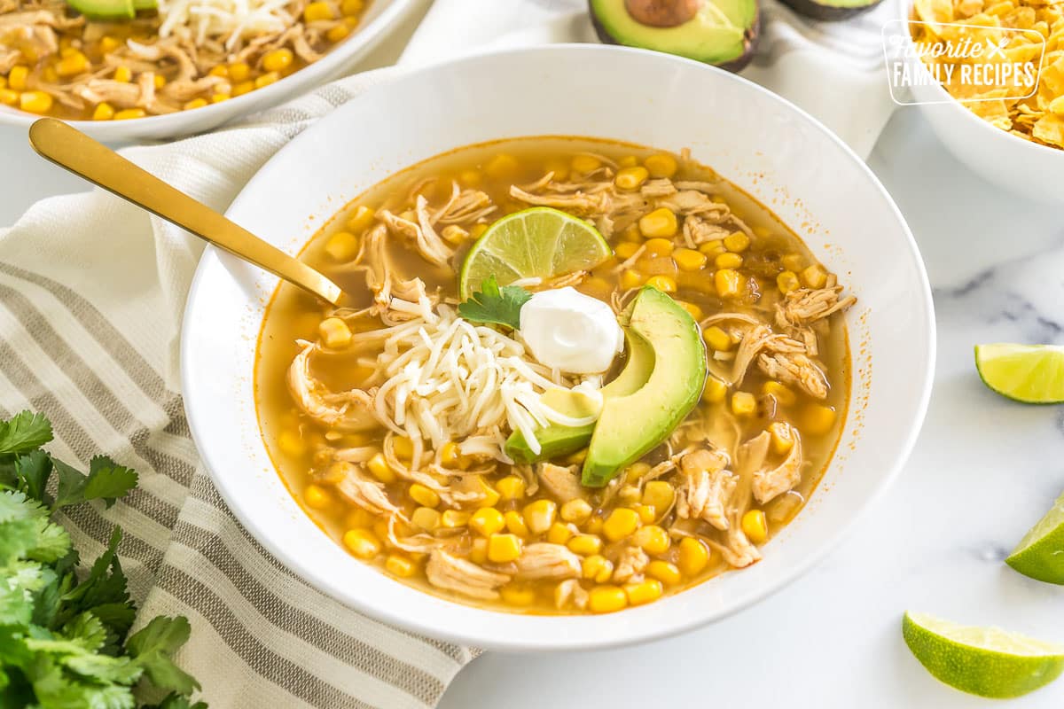 A bowl of chicken tortilla soup topped with lime, sour cream, cheese, and avocado.