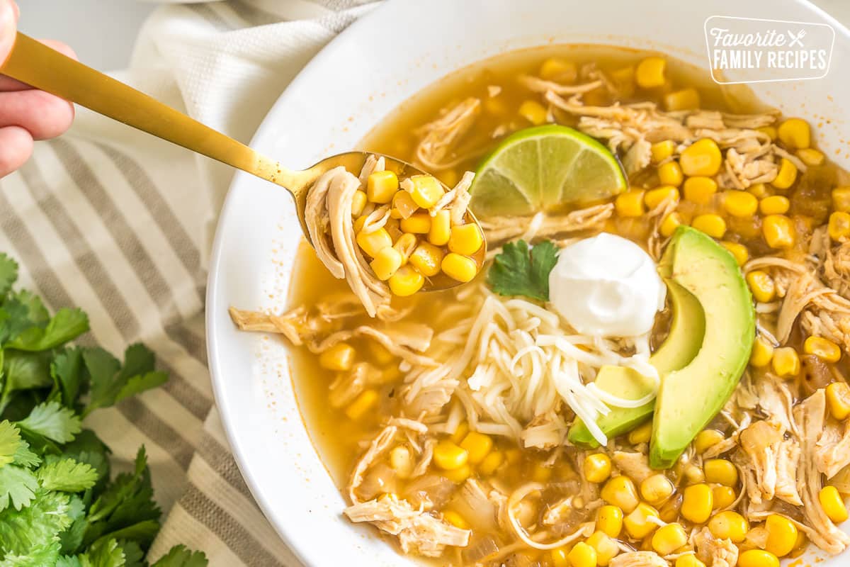 A bowl of chicken tortilla soup topped with lime, sour cream, cheese, and avocado.