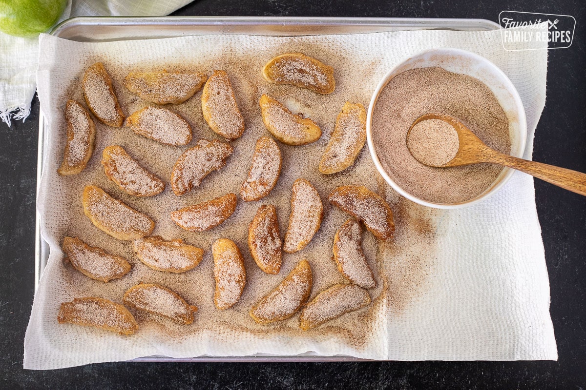 Baking sheet with paper towels and fried apples topped with cinnamon sugar.