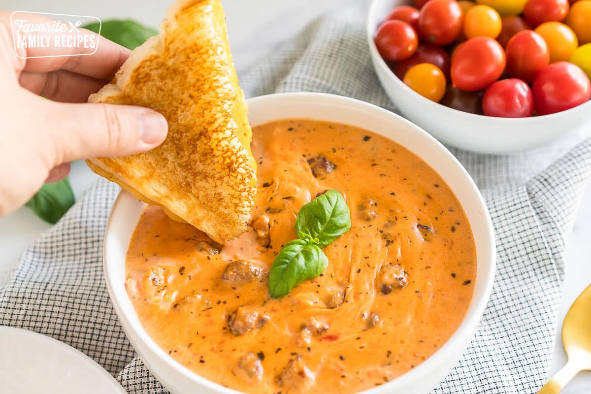 creamy tomato basil soup in a bowl with grilled cheese being dipped in
