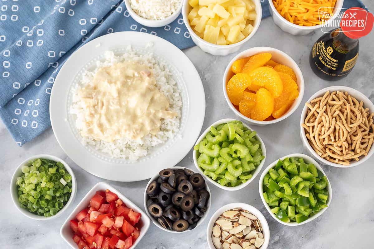 Plate of rice topped with chicken sauce next to all of the toppings for Hawaiian Haystacks.