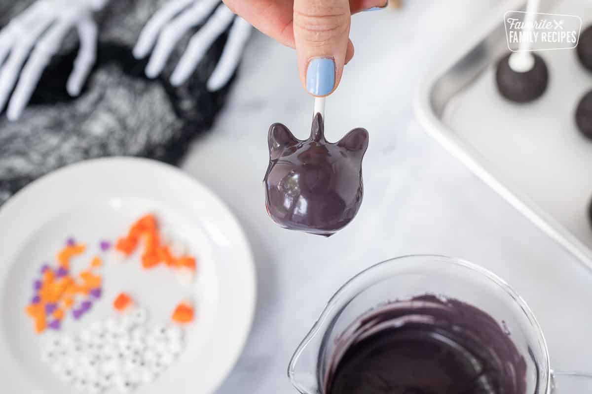 Dipping Halloween black cat cake pop into melted black candy melts.