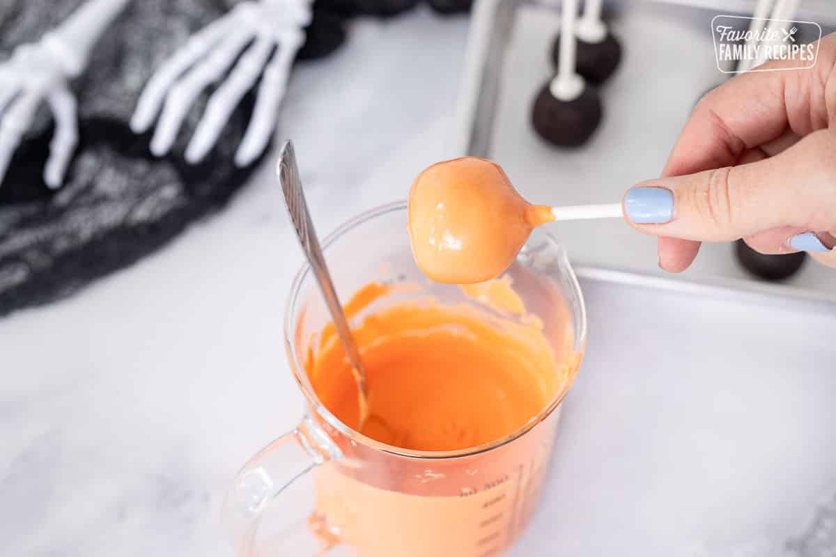 Dipping cake pop in Orange candy melts for a Halloween pumpkin.
