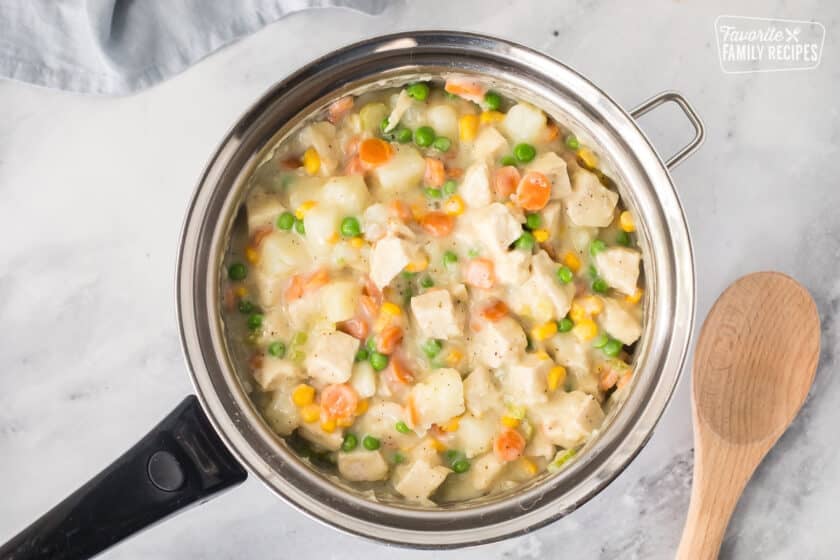 Pot of Homemade Chicken Pot Pie filling next to a wooden spoon.