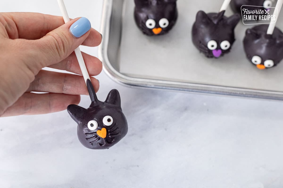 Piping whiskers and mouth onto the black cat Halloween Cake Pops.