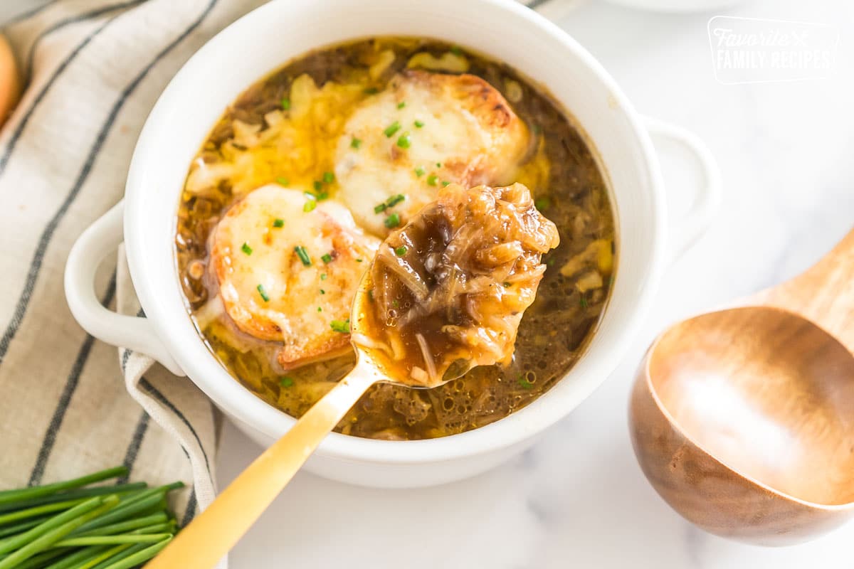 French onion soup in a bowl topped with bread and cheese with a spoonful being scooped out