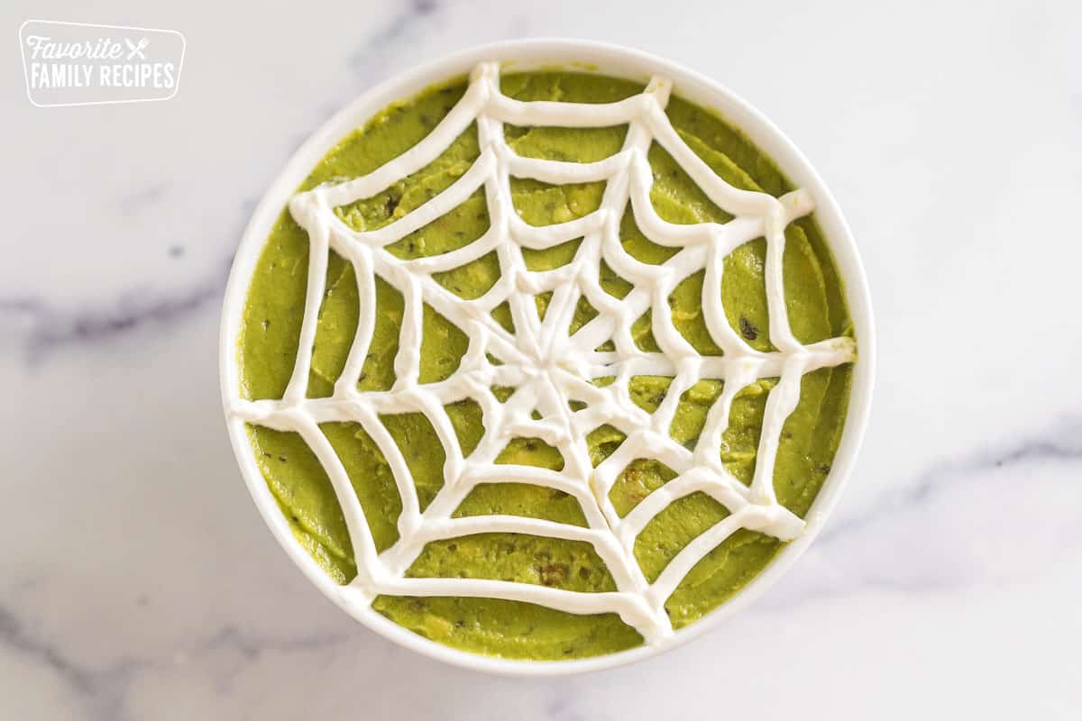 a sour cream spider web on a bowl of guacamole