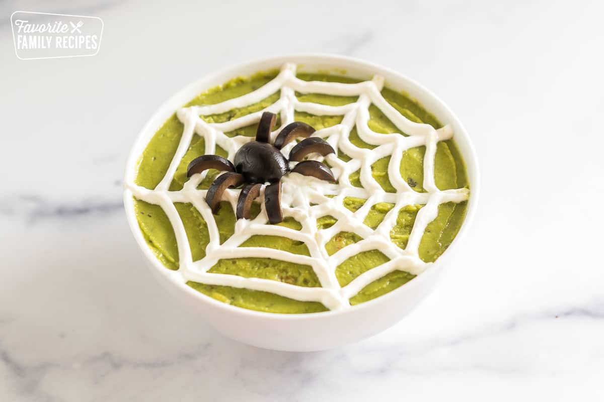 a sour cream spider web on a bowl of guacamole with a spider made of olives