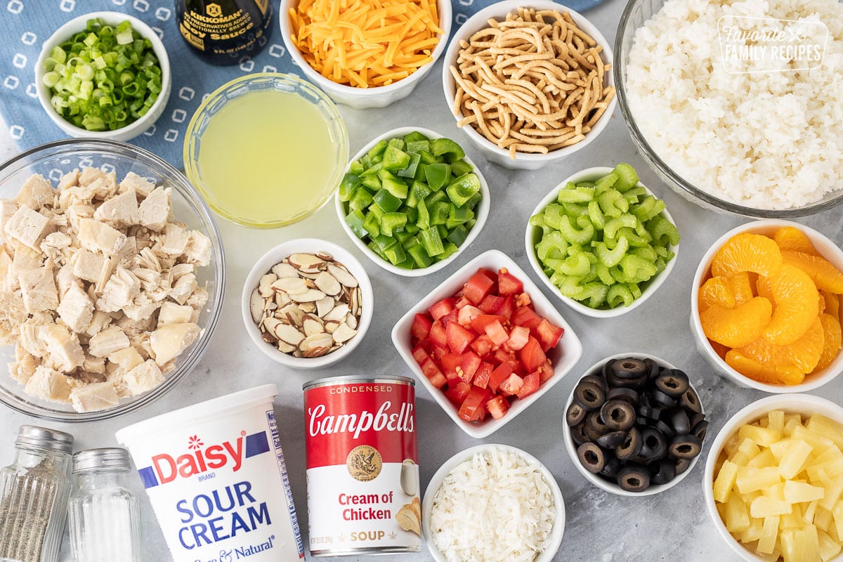 Ingredients to make Hawaiian Haystacks including chicken, sour cream, cream of chicken soup, chicken broth, salt, pepper, green onion, soy sauce, cheese, rice noodles, green peppers, almond slices, tomatoes, celery, black olives, coconut, pineapple, mandarin oranges and rice.