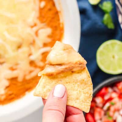 Hand holding a tortilla chip with Restaurant Style Refried Beans and cheese.