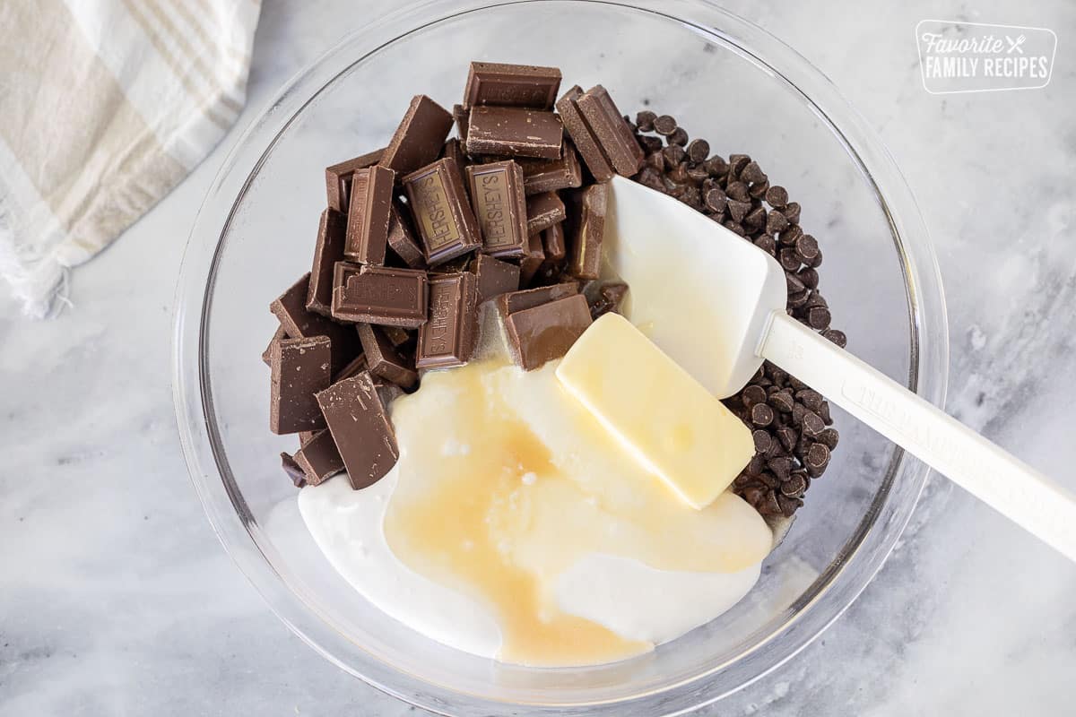 Large glass mixing bowl with Hershey bars, chips, butter and marshmallow creme with hot mixture added.