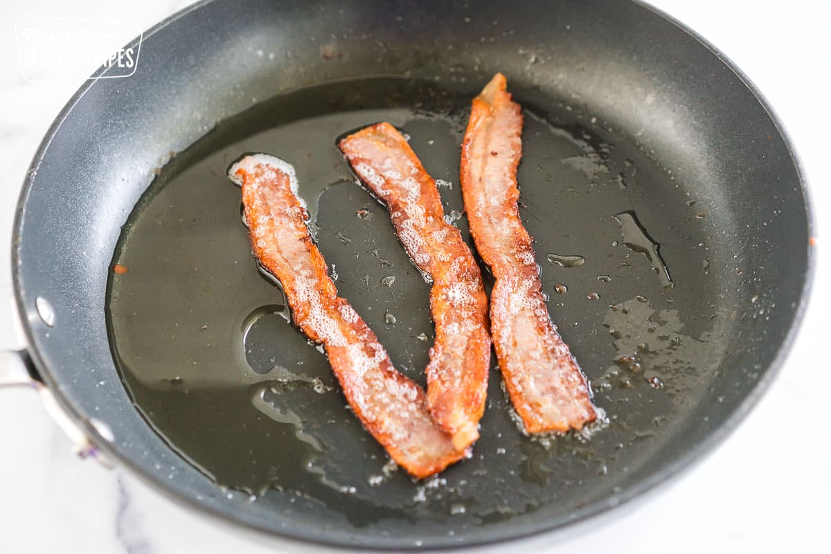 three pieces of bacon cooking in a pan