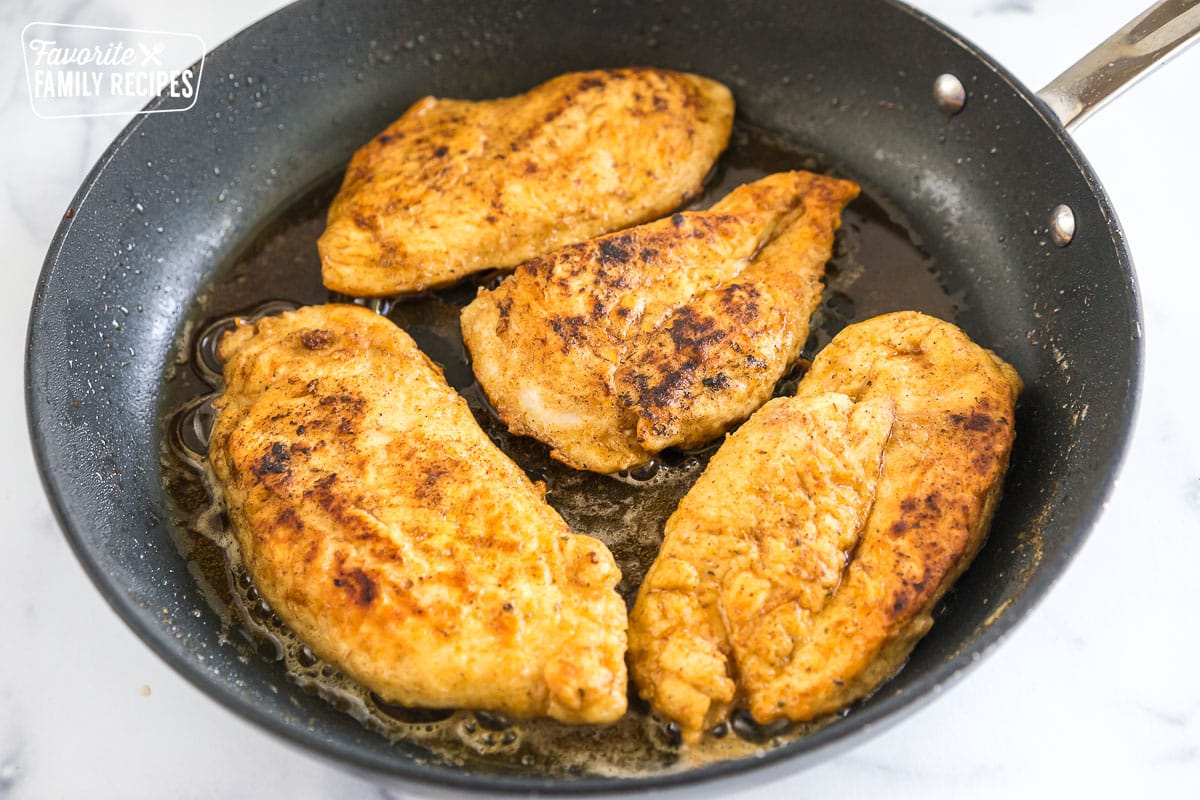 Four pieces of lightly breaded chicken cooking in a skillet