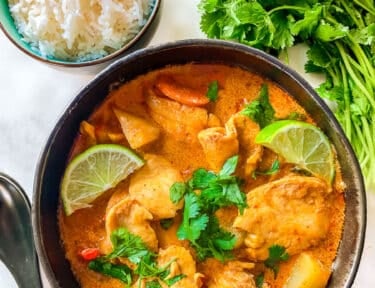 A bowl of Massaman curry with chicken and vegetables next to a bowl of rice