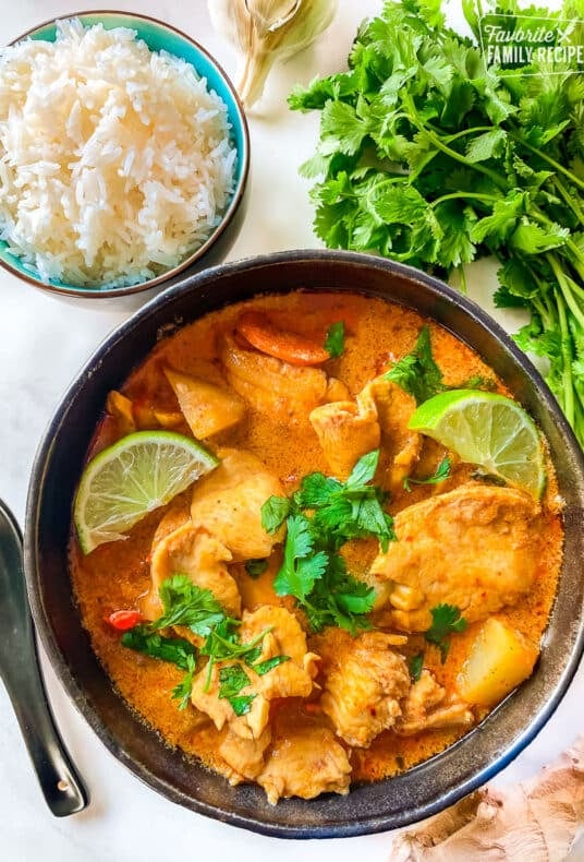 A bowl of Massaman curry with chicken and vegetables next to a bowl of rice.