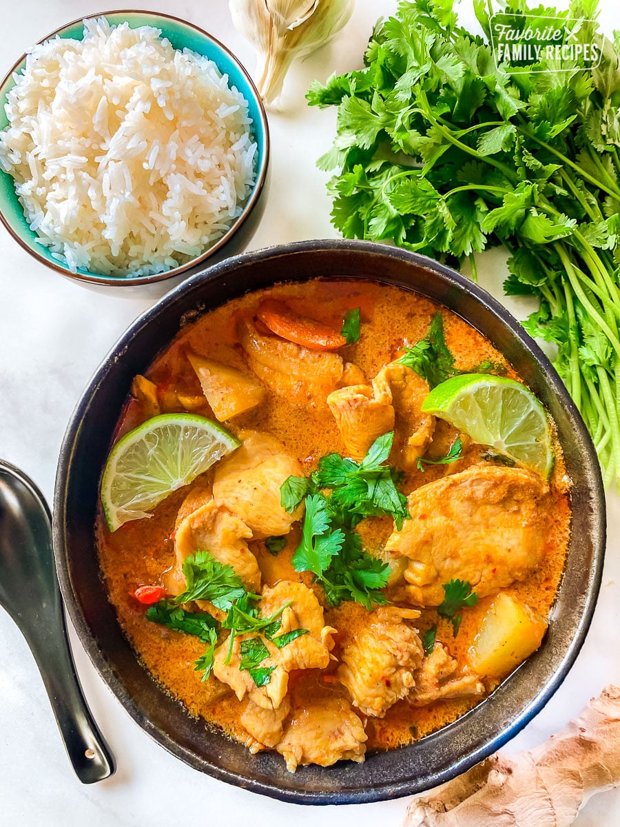 A bowl of Massaman curry with chicken and vegetables next to a bowl of rice.