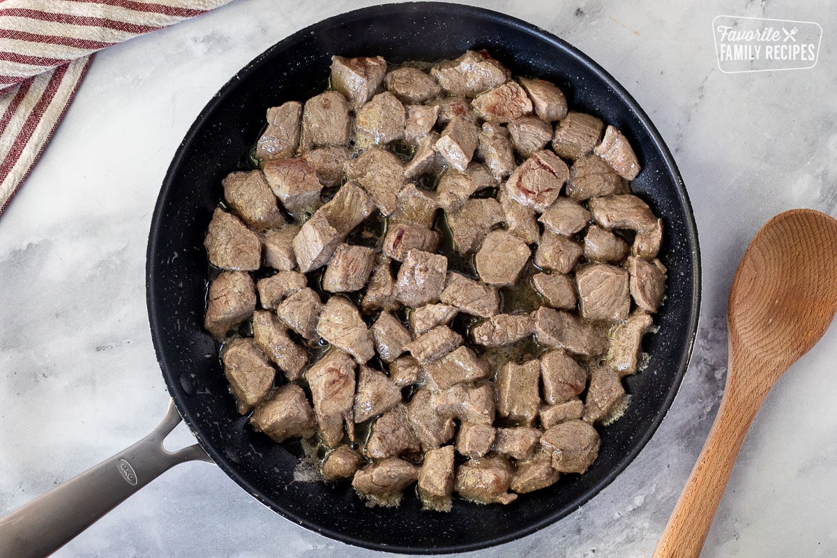 Large skillet with browned cubes of beef for Texas Chili. Wooden spoon on the side.