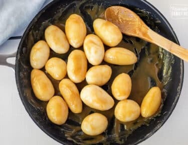 Mixing Brunede Kartofler in a skillet.