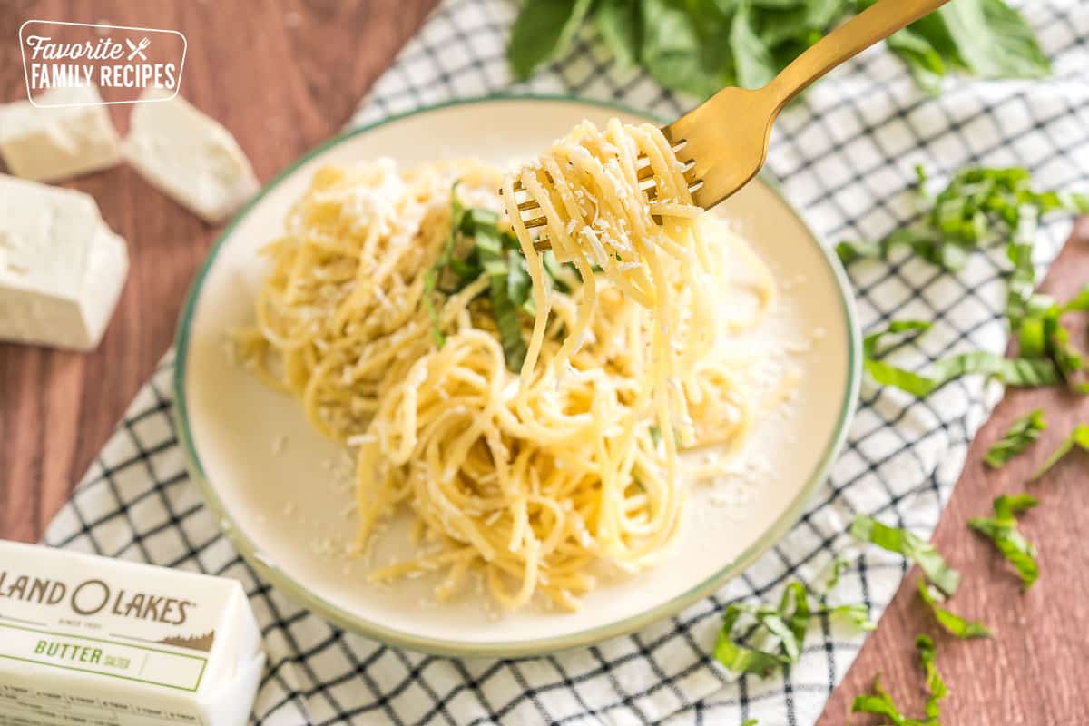 Noodles tossed with brown butter, mizithra cheese, and basil on a plate with a fork taking a bite