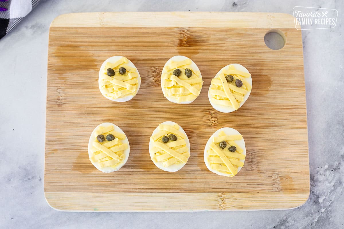 Six mummy Halloween Deviled Eggs on a cutting board.