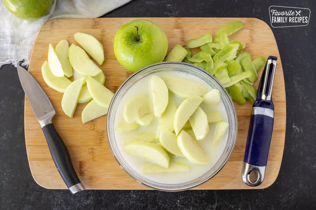 Cutting board with sliced and peeled green apples and a bowl of buttermilk mixture with apples for fries.