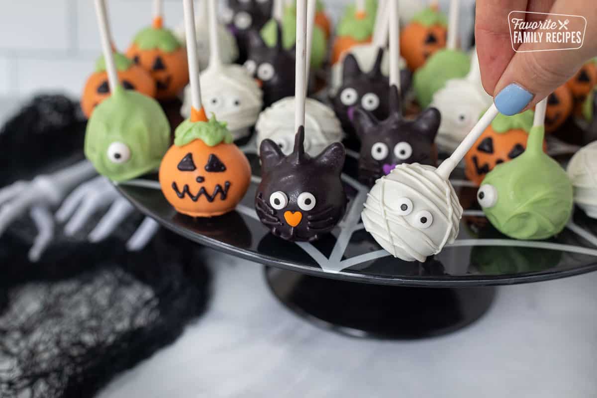 Hand picking up a mummy Halloween Cake Pop from stand.