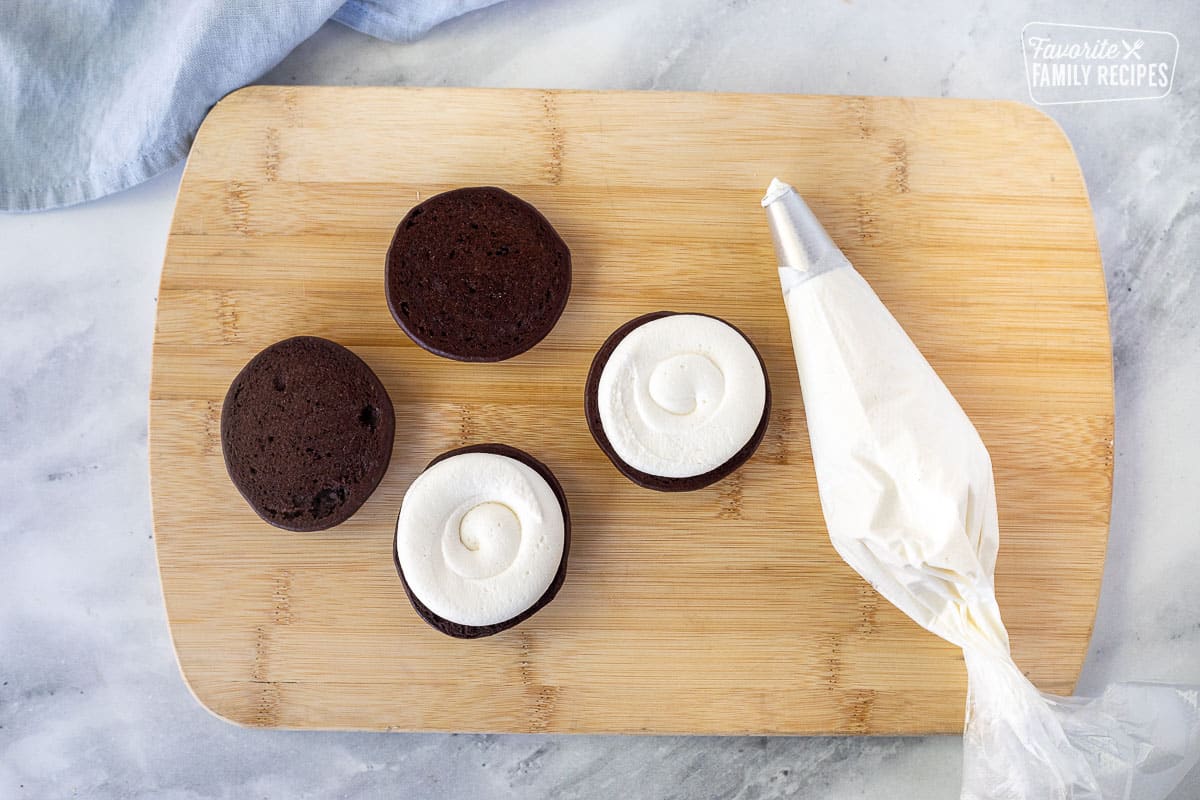 Board with piping bag and two Whoopie Pie cookies piped with marshmallow frosting in swirl pattern.