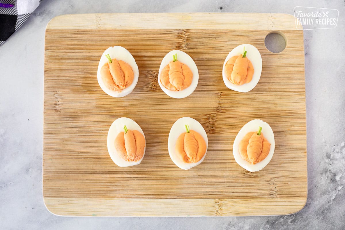 Six pumpkin Halloween Deviled Eggs on a cutting board.