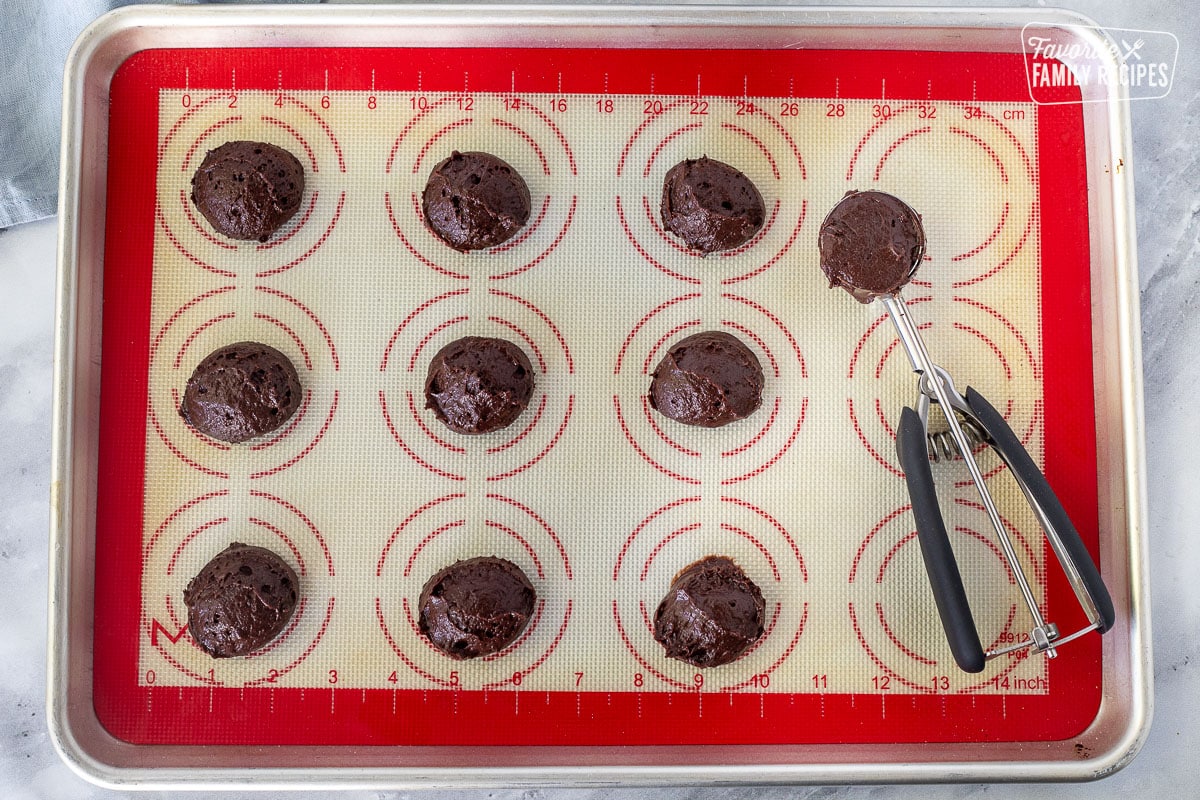 Baking sheet with silicone baking mat and scooped balls of Whoopie Pie dough next to cookie scoop.