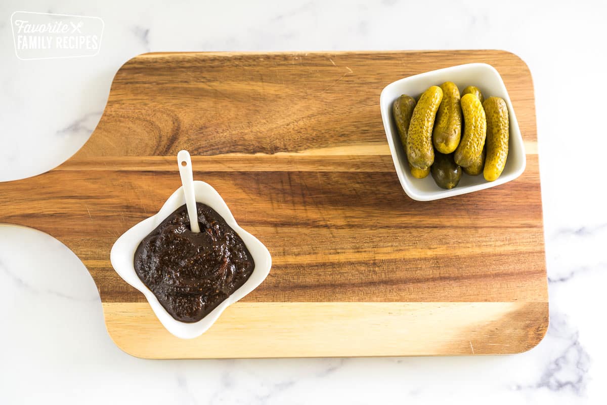 a bowl of fig butter and a bowl of pickles on a wooden slab