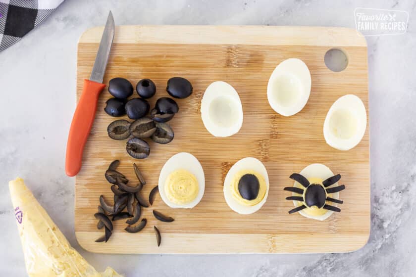 Cutting board with stages for making Spider Halloween Deviled Eggs with black olives.