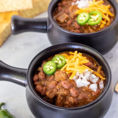 Two bowls of Texas Chili with cheese, onion and jalapeños on the top. Cornbread on the side.