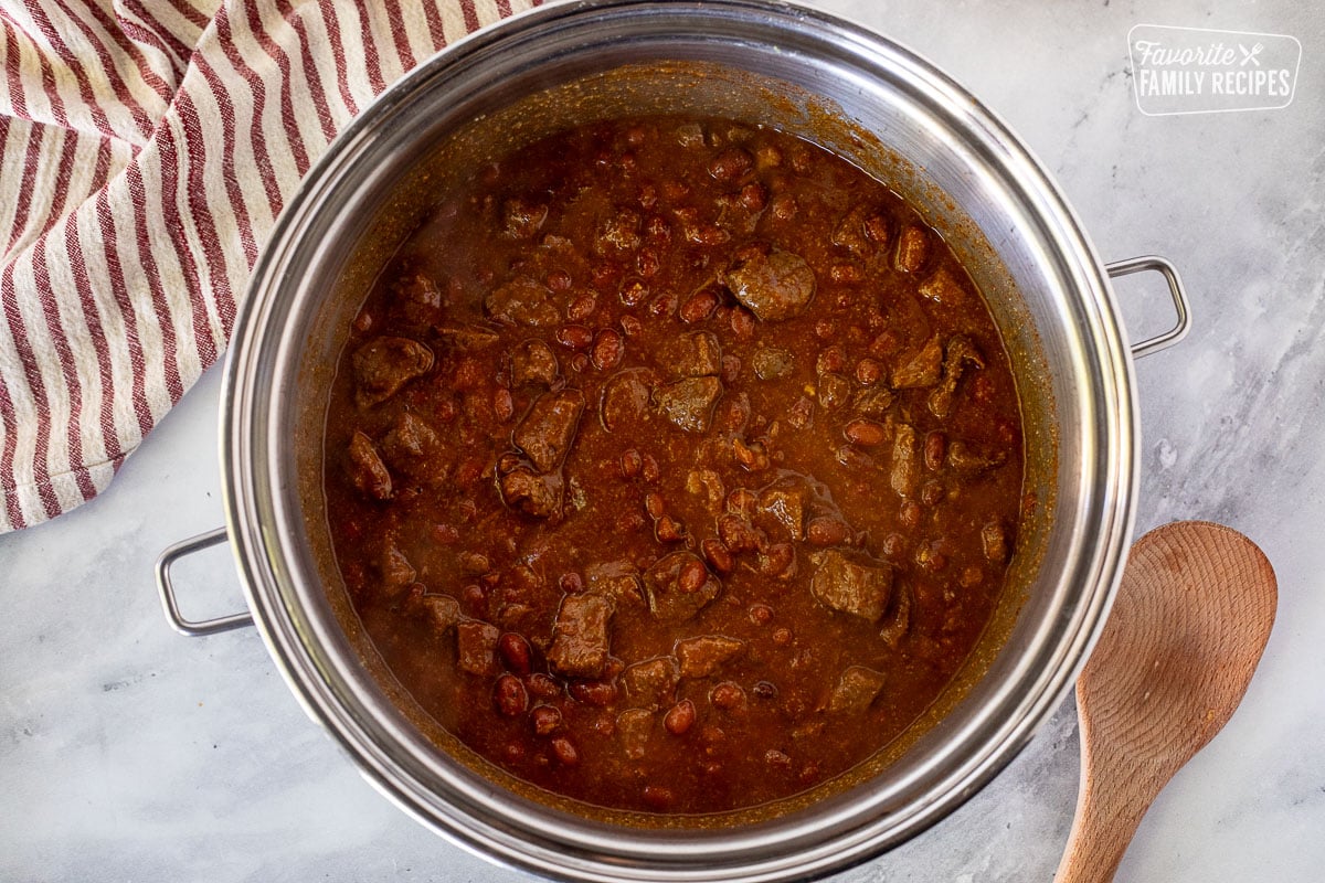 Cooked Texas Chili in a large pot. Wooden spoon on the side.