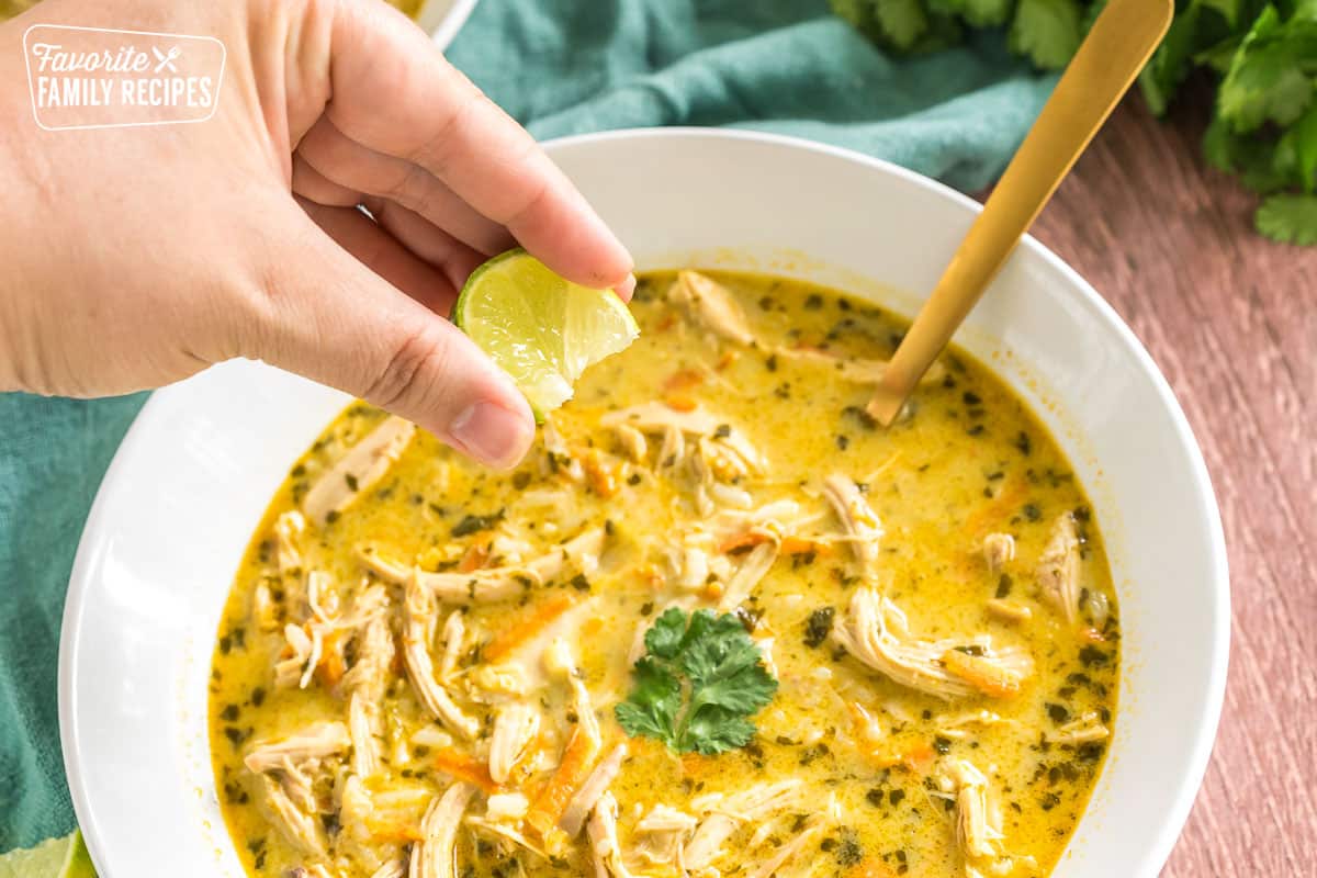 a hand squeezing a lime wedge into a bowl of soup