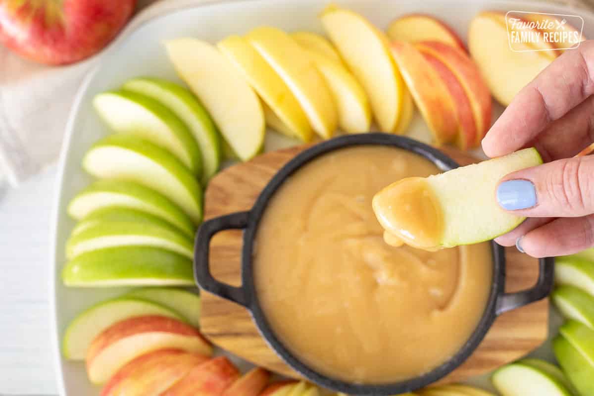 Hand holding a green apple slice with Caramel dip.