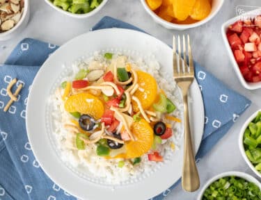 Constructed Hawaiian Haystack topped with green onion, cheese, rice noodles, green peppers, almond slices, tomatoes, celery, black olives, coconut, pineapple and mandarin oranges.