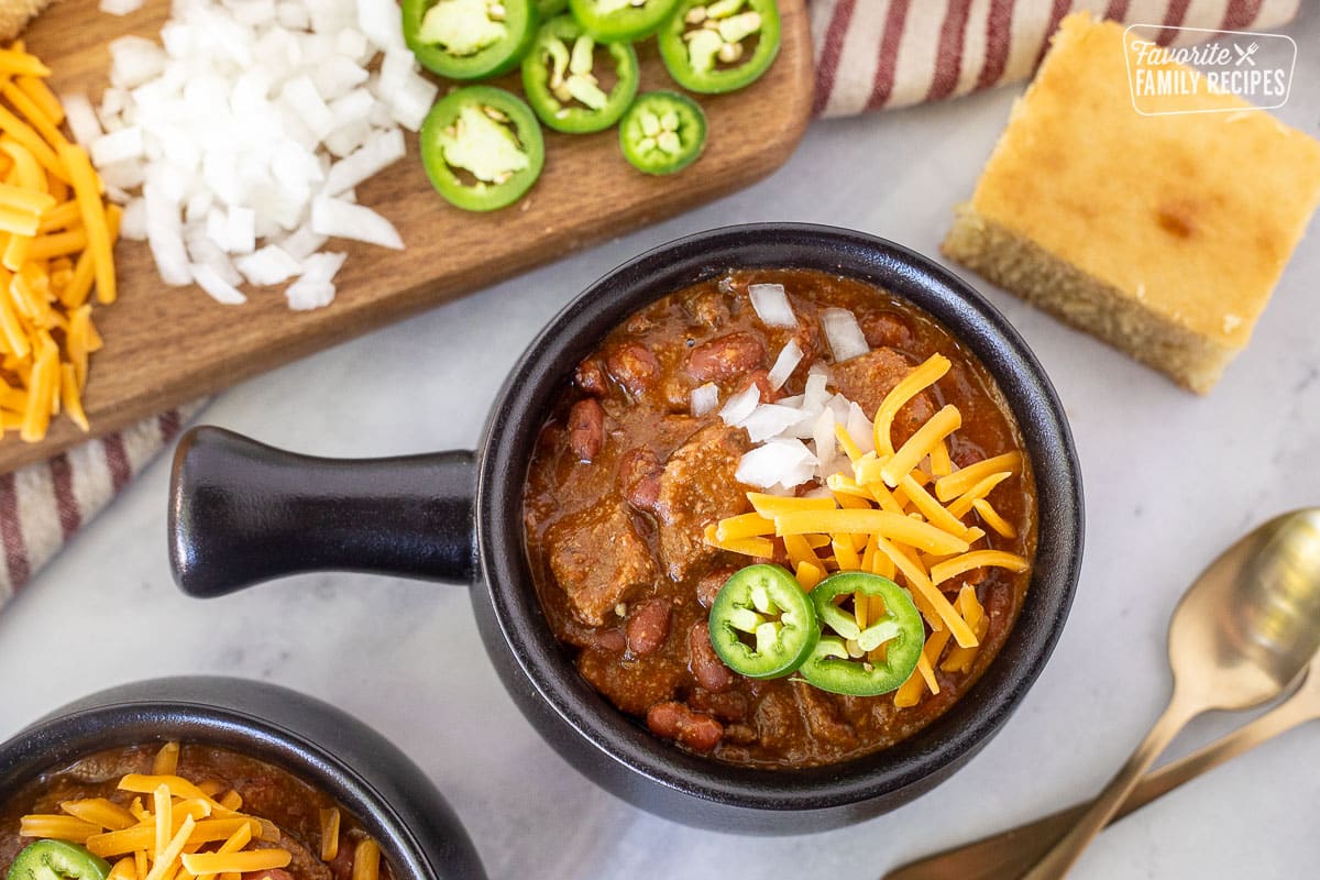 Bowl of Texas Chili in a bowl with shredded cheddar cheese, chopped white onions and sliced jalapeños.