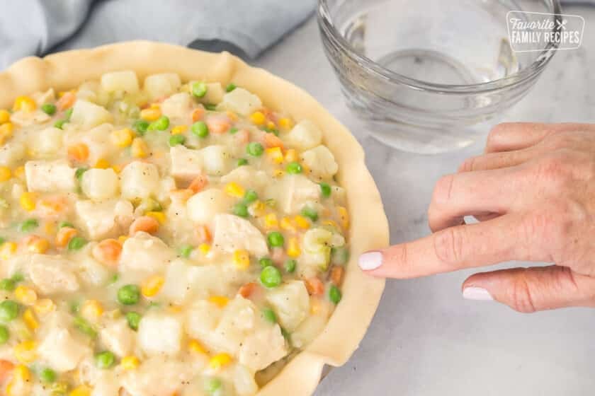 Rubbing water around the rim of the pie crust for Homemade Chicken Pot Pie.