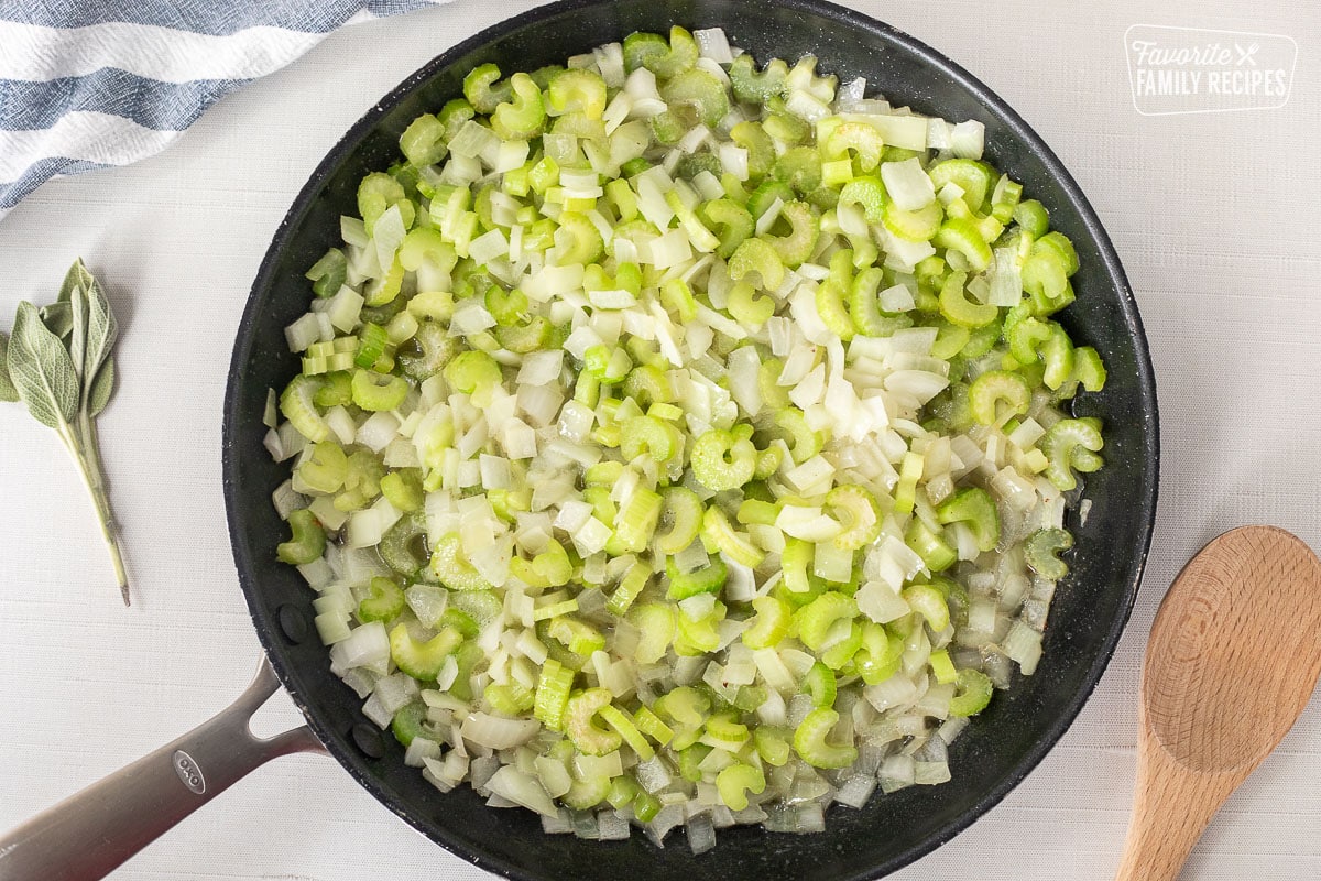 Skillet with diced celery and onion. Wooden spoon on the side.