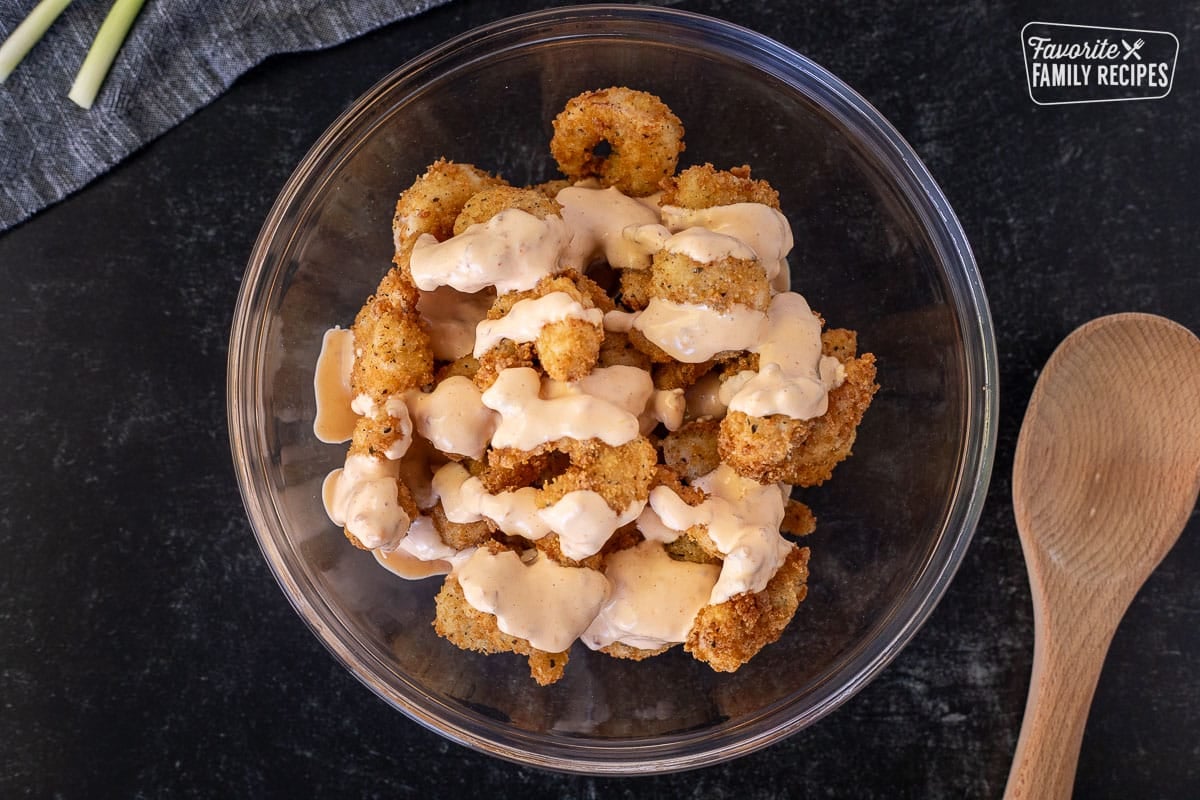 Mixing bowl with fried shrimp and sauce on top. Wooden spoon on the side.