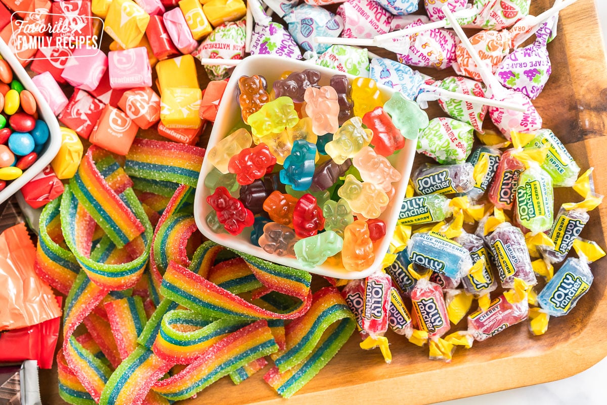 a bowl of gummy bears surrounded by lollipops, jolly ranchers, starbursts, and sour ribbons