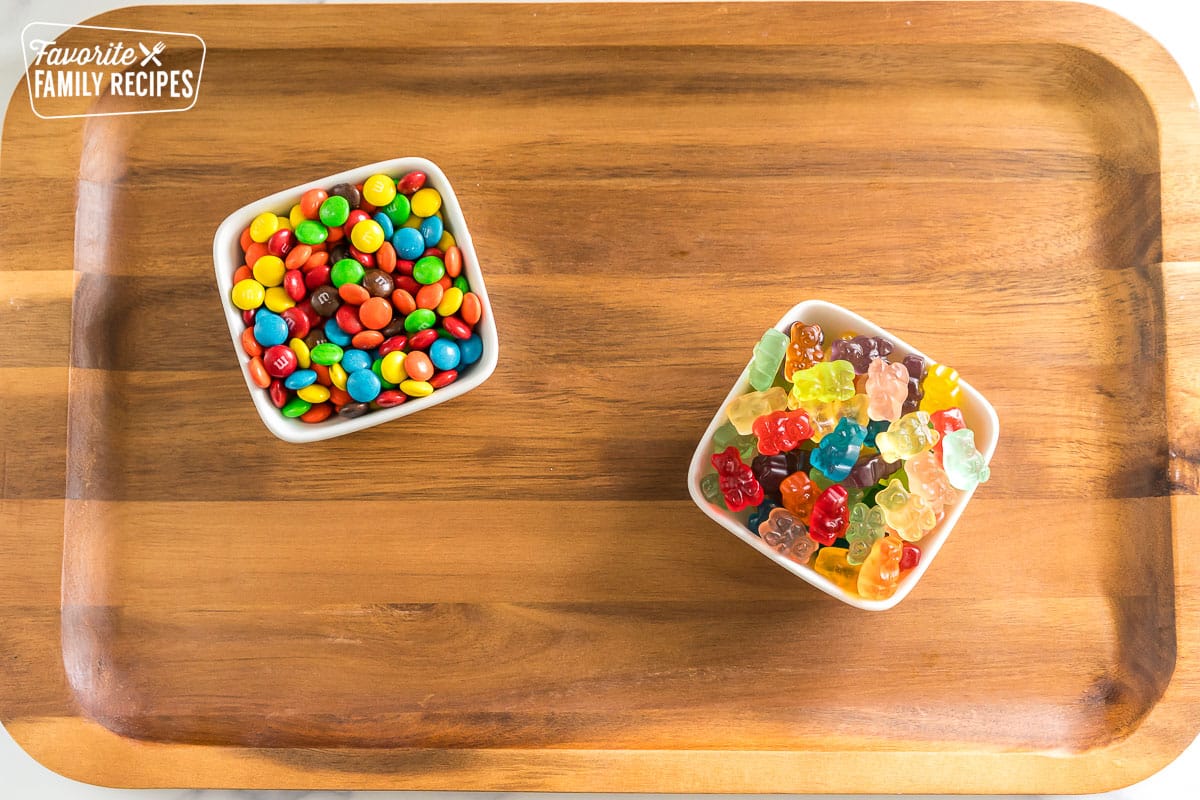 a wooden board with two small bowls of candy on it