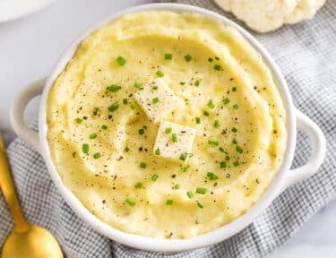 a bowl of cauliflower mashed potatoes topped with butter, pepper, and chives