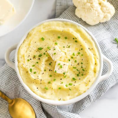 a bowl of cauliflower mashed potatoes topped with butter, pepper, and chives