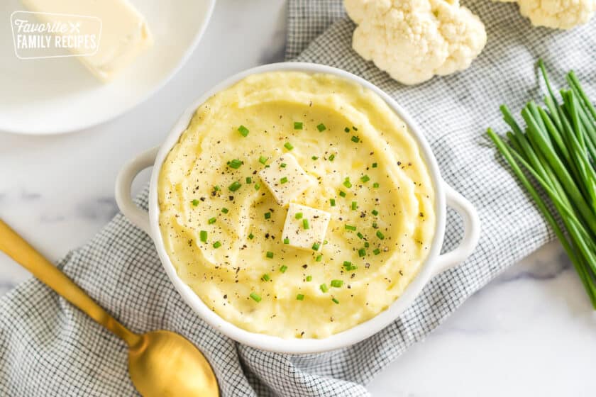 a bowl of cauliflower mashed potatoes topped with butter, pepper, and chives