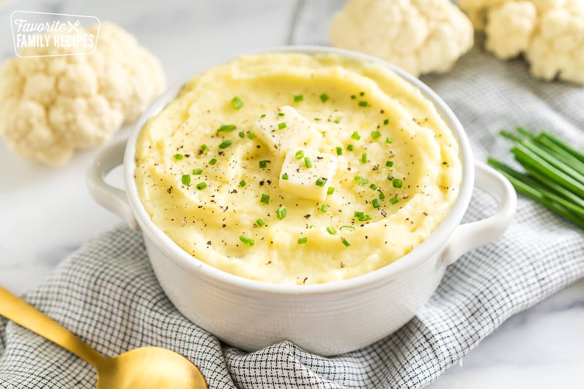 A bowl of cauliflower mashed potatoes topped with butter, pepper, and chives.